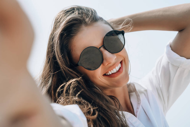 Κοντινό-up της νεαρής όμορφη γυναίκα σε γυαλιά ηλίου χαμογελαστά κρατώντας  - Φωτογραφία, εικόνα