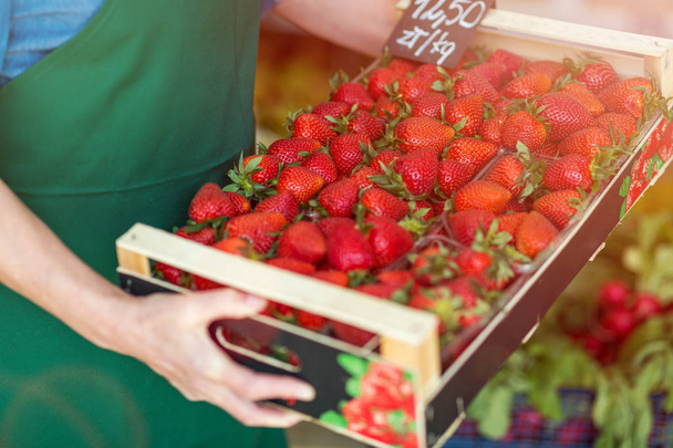 Shop assistant holding box with fresh strawberries in organic produce shop - Photo, image