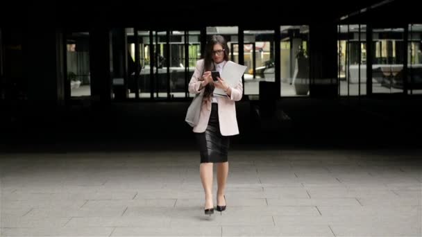 Mladá úspěšná brunetka obchodní žena prochází městem s dokumenty a používá telefon Smartphone. - Záběry, video
