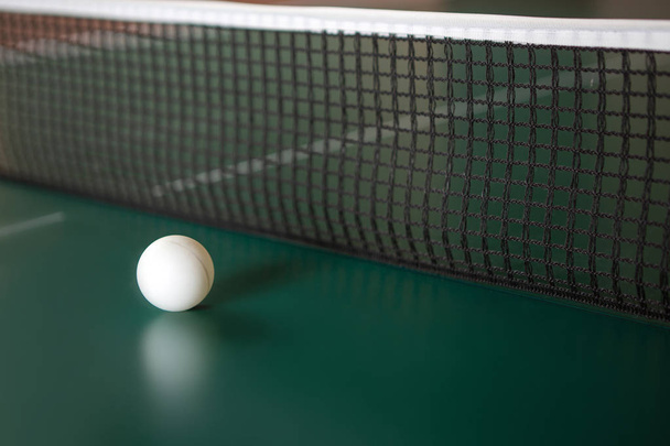 ein Tischtennisball auf einem grünen Tisch neben dem Netz.  - Foto, Bild