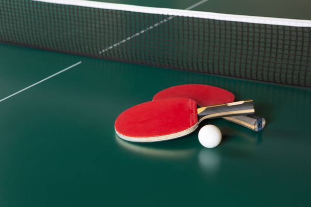 Twee pingpong rackets en een bal op een groene tafel. Ping-Pong netto - Foto, afbeelding