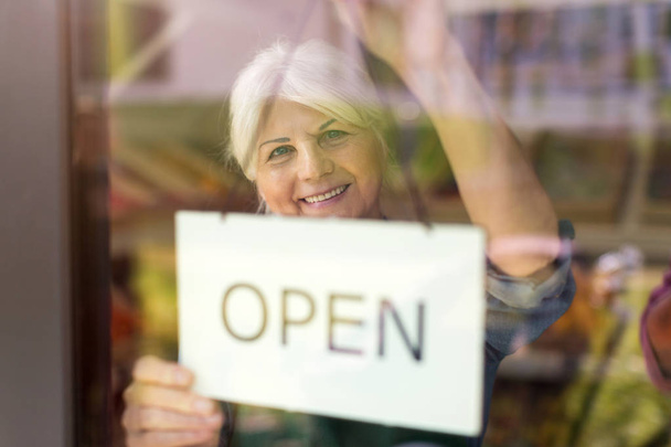 Ανώτερη γυναίκα που κρατά ανοιχτή πινακίδα στο κατάστημα βιολογικών προϊόντων - Φωτογραφία, εικόνα