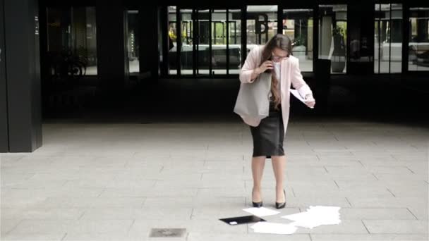 Eine junge, gestresste Geschäftsfrau mit Brille geht mit Dokumenten und Telefongesprächen durch die Stadt. Sie lässt aus Stress ihre Papiere fallen. - Filmmaterial, Video