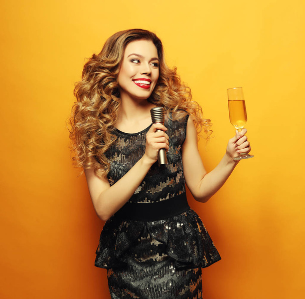woman in black evening dress holding glass of champagne and microphone. Ready for karaoke party. - Photo, Image