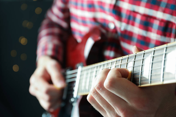 Man spelen op elektrische gitaar tegen donkere achtergrond, close-up - Foto, afbeelding