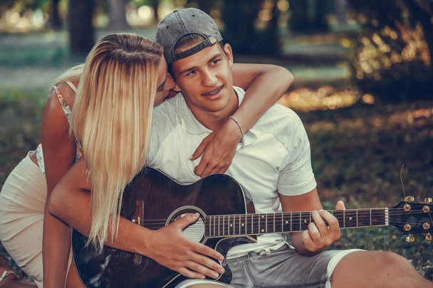 Νεαρό ζευγάρι που διασκεδάζουν με την κιθάρα κατά τη διάρκεια πικνίκ στο πάρκο - Φωτογραφία, εικόνα