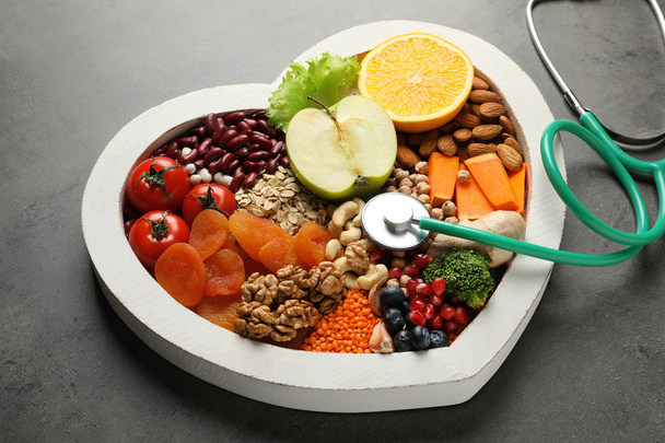 Heart shaped tray with healthy products and stethoscope on grey background - Fotó, kép