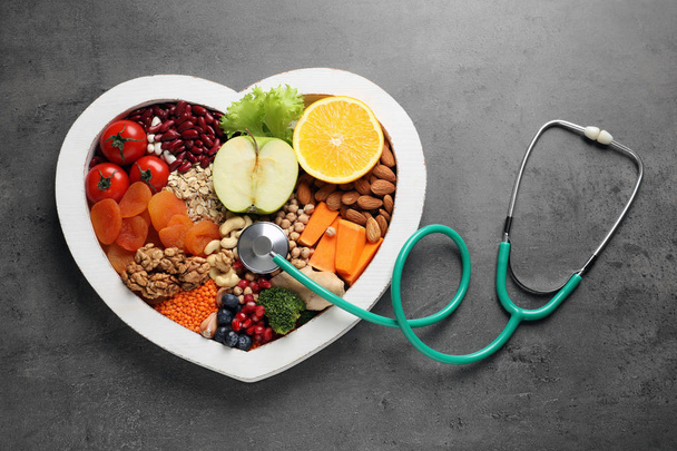 Heart shaped tray with healthy products and stethoscope on grey background, top view - 写真・画像