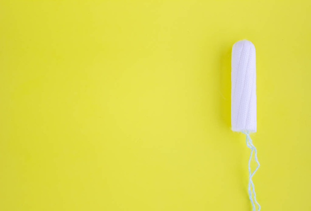 One swab with cotton on a yellow background. The concept of the period of the menstrual cycle. Top view, flat lay. - Photo, Image