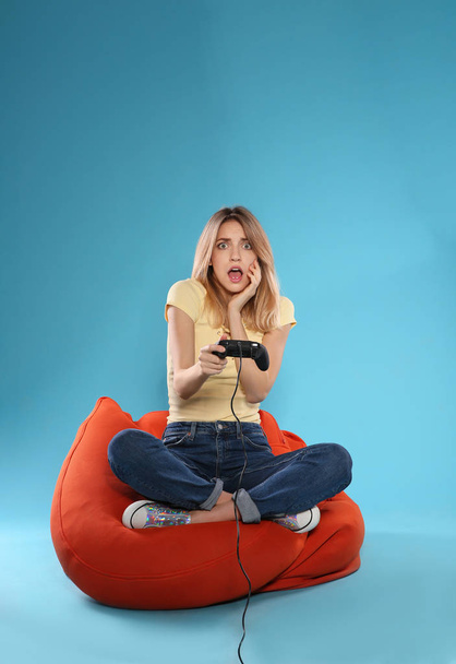 Emotional young woman playing video games with controller on color background. Space for text - Φωτογραφία, εικόνα