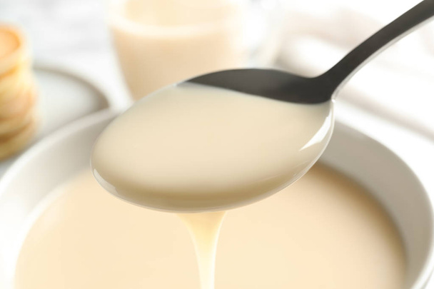 Spoon of pouring condensed milk over bowl, closeup. Dairy products - Fotografie, Obrázek