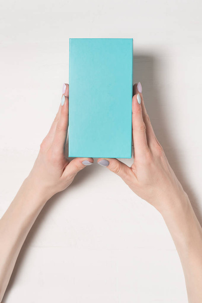 女性の手で長方形のターコイズ ブルー ボックス。平面図です。背景に白いテーブル - 写真・画像
