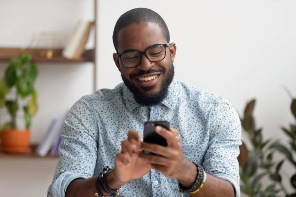 Happy african american businessman using phone mobile apps at workplace - Photo, Image