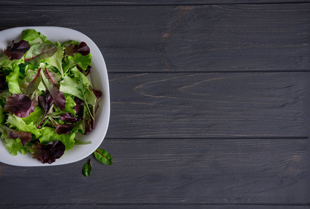 Template for a banner with a plate of green salad on a gray wooden background. Healthy food, vegetarians, diet. Basis for a banner with a plate of green salad. View from above - Fotografie, Obrázek