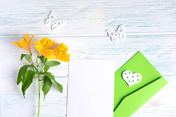 Mock up blank paper and envelope on white wooden background with natural flowers of yellow color. Blank, frame for text. Greeting card design with flowers. Flat lay, top view. - Foto, Imagen
