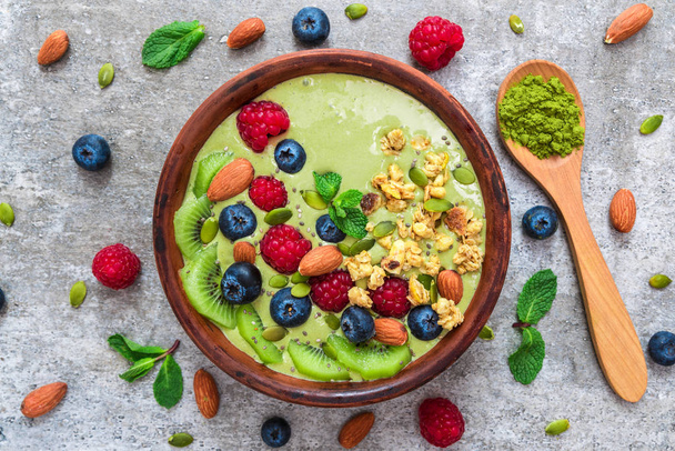matcha green tea smoothie bowl with fresh fruits, berries, nuts, seeds and granola with a spoon for healthy breakfast - Photo, Image