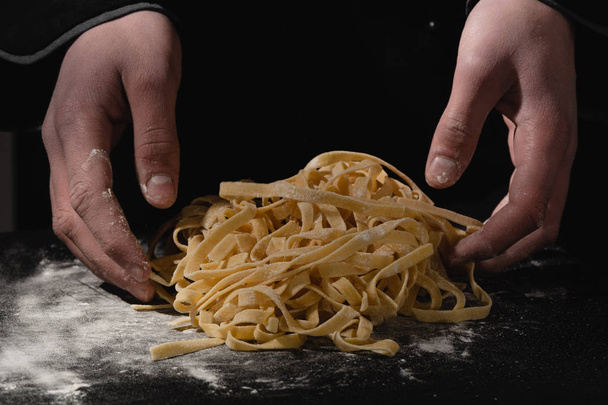 Küchenchef Hände Herstellung von Spaghetti, Nudeln, Nudeln mit frischen Nudeln auf schwarzem Tisch mit. - Foto, Bild