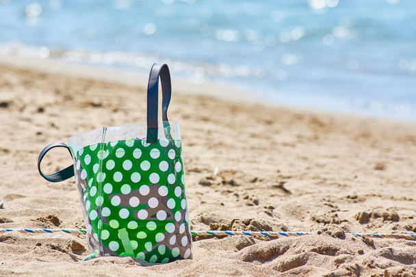 Borsa da spiaggia verde con piselli bianchi per il trasporto di asciugamani e documenti in piedi sulla spiaggia sabbiosa
 - Foto, immagini