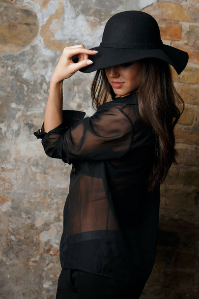 Привлекательная брюнетка модель в шляпе и черной блузке позирует не
 - Фото, изображение