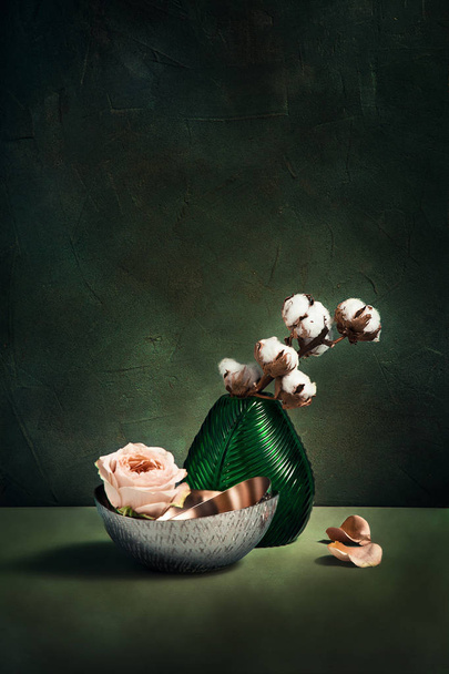Lähikuva koriste puuvilla vihreä lasi maljakko vastaan kuvioitu betoniseinä. Hollannin asetelma modernilla sisustuksella. Minimalismi käsite kukkakauppa. Puuvilla ja ruusu. onnittelukortti
 - Valokuva, kuva