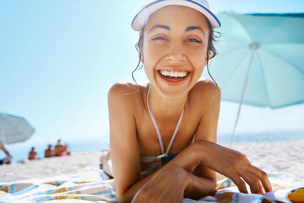 portrait of beautiful smiling happy woman tanning in white cap on sandy beach at summer. Summer vacation concept. - Φωτογραφία, εικόνα