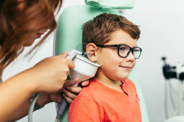 Young boy at medical examination or checkup in otolaryngologist's office. Ear irrigation and earwax removal.  - Photo, image
