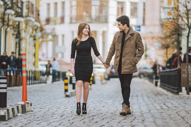 Urban modern young love couple walking romantic talking talking, holding hands on a date. Young multicultural Turkish brunette and Caucasian couple on old european street. Autumn spring weather - Zdjęcie, obraz
