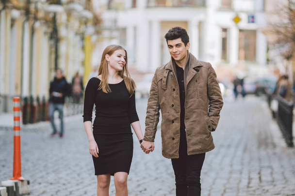 Urban modern young love couple walking romantic talking talking, holding hands on a date. Young multicultural Turkish brunette and Caucasian couple on old european street. Autumn spring weather - Foto, Bild