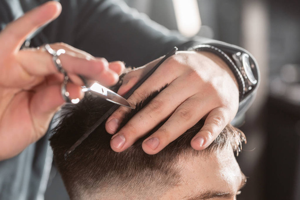 Close-up Hair cutting with metal scissors. Master cuts hair and beard of men in the barbershop, hairdresser makes hairstyle for a young man - Photo, image