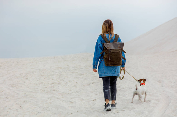 Reizen meisje met rugzak en hond op een zandstrand in lente tijd - Foto, afbeelding