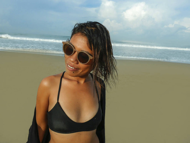 lifestyle portrait of young beautiful and sexy Asian girl in bikini and sunglasses enjoying holidays at tropical beach posing cool and confident at the sea - 写真・画像