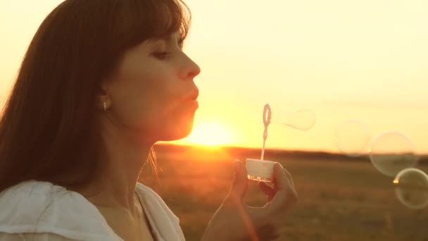 щаслива дівчина дме красиві мильні бульбашки в парку на узбережжі навесні, влітку і посміхається. Повільний рух. молода дівчина відпочиває на сонці
. - Кадри, відео