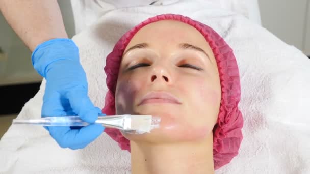 Gyönyörű nő arcpakolás a szépségszalonban. Alkalmazása arc maszkot a női arc bőrgyógyászati klinikán. Spa terápiás eljárás a fiatal nő. Kozmetikus alkalmazása arcpakolás. Hd - Felvétel, videó