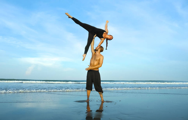 young attractive and beautiful acrobat couple practicing acroyoga exercise concentrated keeping balance practiing yoga on the beach in relaxation and meditation concept - Valokuva, kuva