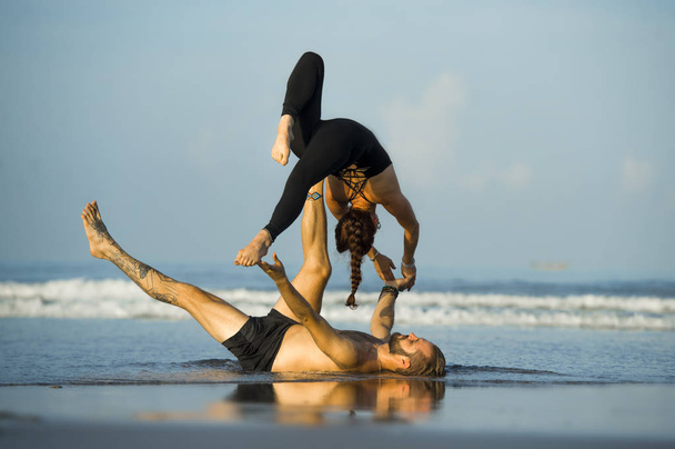 young attractive and beautiful acrobat couple practicing acroyoga exercise concentrated keeping balance practiing yoga on the beach in relaxation and meditation concept - Zdjęcie, obraz