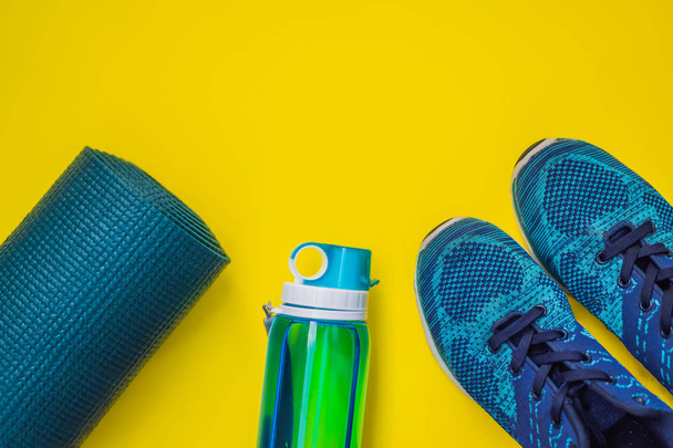 Everything for sports turquoise, blue shades on a yellow background. Yoga mat, sport shoes sportswear and bottle of water. Concept healthy lifestyle, sport and diet. Sport equipment. Copy space - Foto, imagen