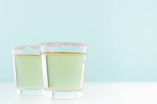 Refreshment rich alcohol shot drinks of golden tequila with salt rim on white and pastel green background, copy space. - Фото, зображення