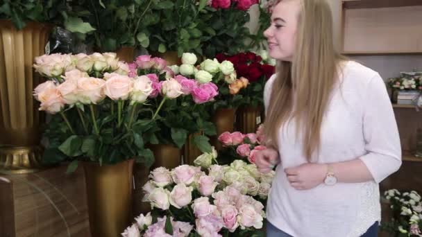 Κορίτσι ανθοπώλης ψάχνει για λουλούδια και επιλέγει τρία όμορφα φρέσκα τριαντάφυλλα για ένα μπουκέτο σε ένα ανθοπωλείο . - Πλάνα, βίντεο