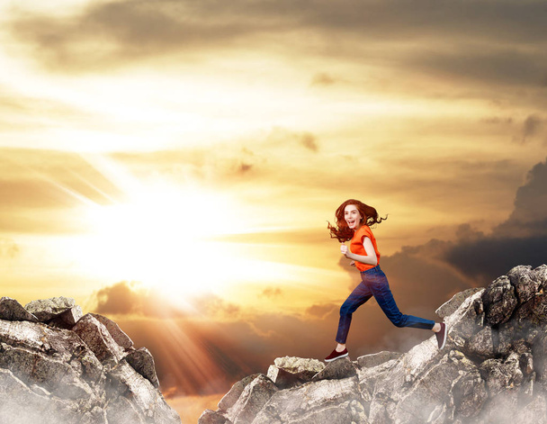 Redhead woman jumps over cliff on blue sky background. - Photo, Image