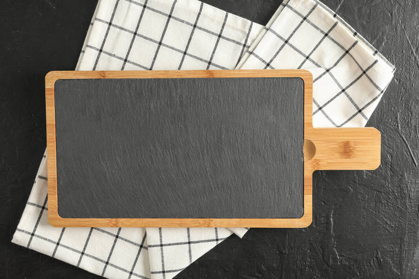 Tabla de cortar con toalla de cocina sobre fondo negro, vista superior
 - Foto, Imagen