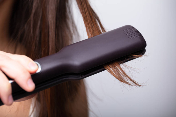 Close-up Of Woman Straightening Hair With Straightener Against Gray Background - Fotó, kép