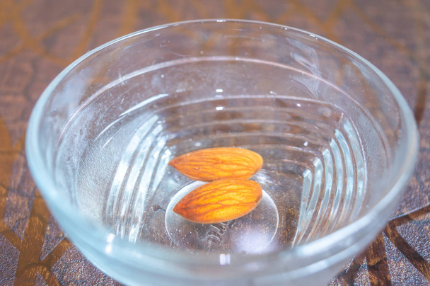 Almonds kept in a glass bowl containing water. Peeling of almond skin in progress - Photo, Image