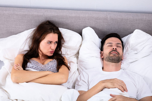 Dühös fiatal nő nézett ember horkolás az ágyban otthon - Fotó, kép