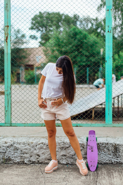 Summer lifestyle image of trendy pretty young girl standing next to the scateboard coart with her plastic scateboard. - Foto, immagini