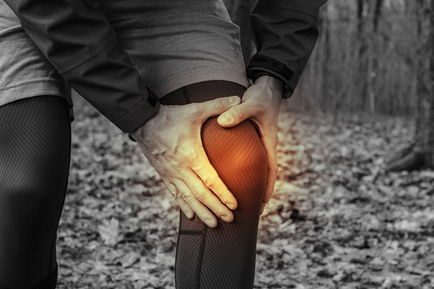 A man in training clothes got a knee injury while jogging in outdoor workout. Concept of sports injury, running technique, wrong running, tendonitis, a large load. - Photo, Image