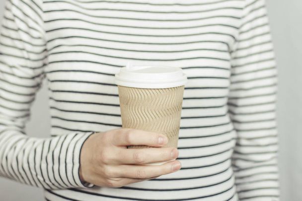 Дівчина в смугастій футболці тримає паперову чашку з кавою або чаєм перед нею. Концепція вилучення їжі, кав'ярня
. - Фото, зображення