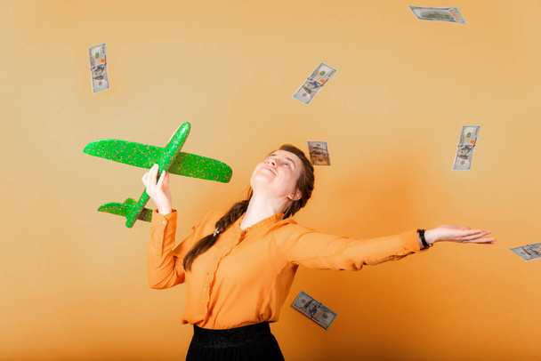 Dziewczyna rzuca dolarów na bok i posiada zielony samolot w ręku, znak wolności i niezależności finansowej. - Zdjęcie, obraz