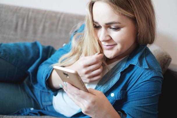 Portrait of dreamy thoughtful woman lying on couch holding smart phone - Photo, Image