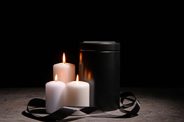 Mortuary urn, burning candles and black ribbon on table against dark background - Photo, Image