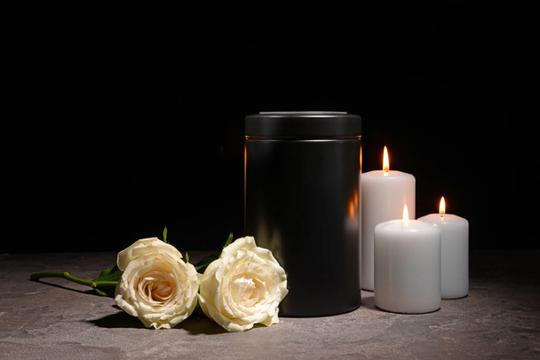 Mortuary urn, burning candles and flowers on table against dark background - Photo, Image